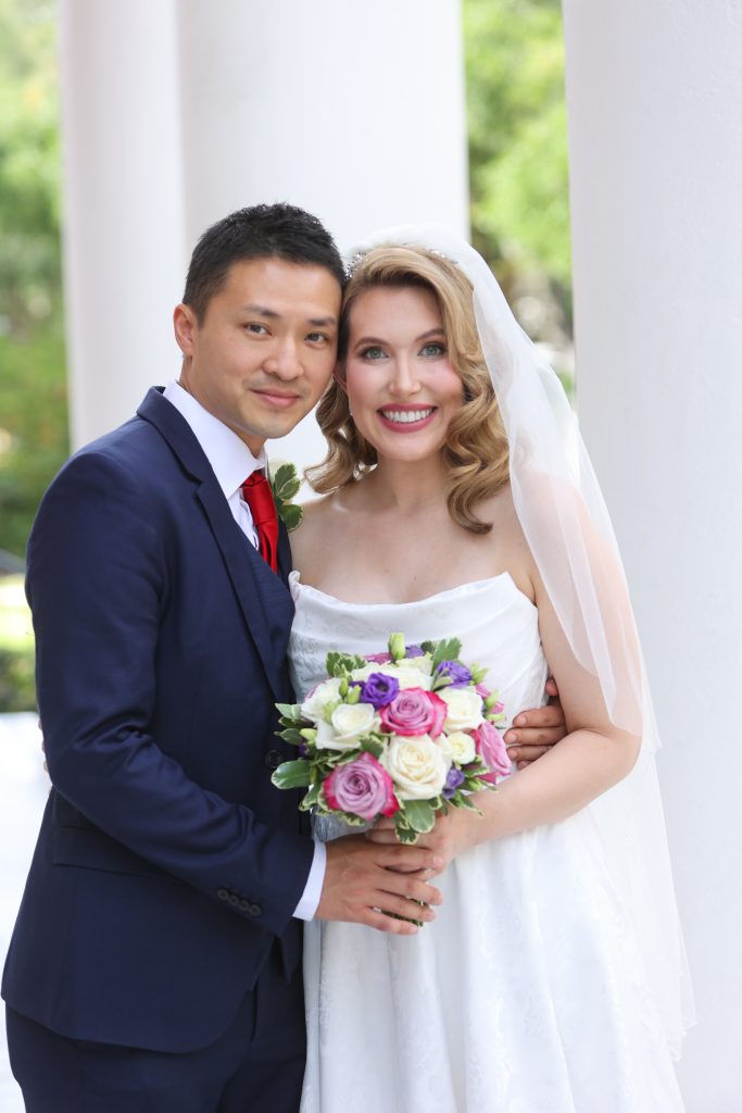 Braut und Bräutigam lächelnd mit Blumenstrauß in der Hand