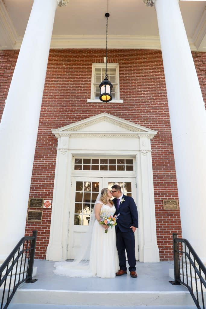Newlyweds Leila and Derrick kissing in front of the white-columned entrance of First Congregational Church.